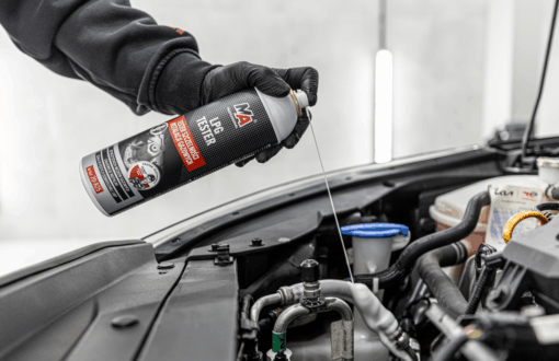 Osoba w czarnej rękawiczce aplikuje preparat MA Professional LPG Tester do układu klimatyzacji w komorze silnika samochodu. Aerozol jest rozpylany bezpośrednio na elementy instalacji w celu wykrywania nieszczelności.